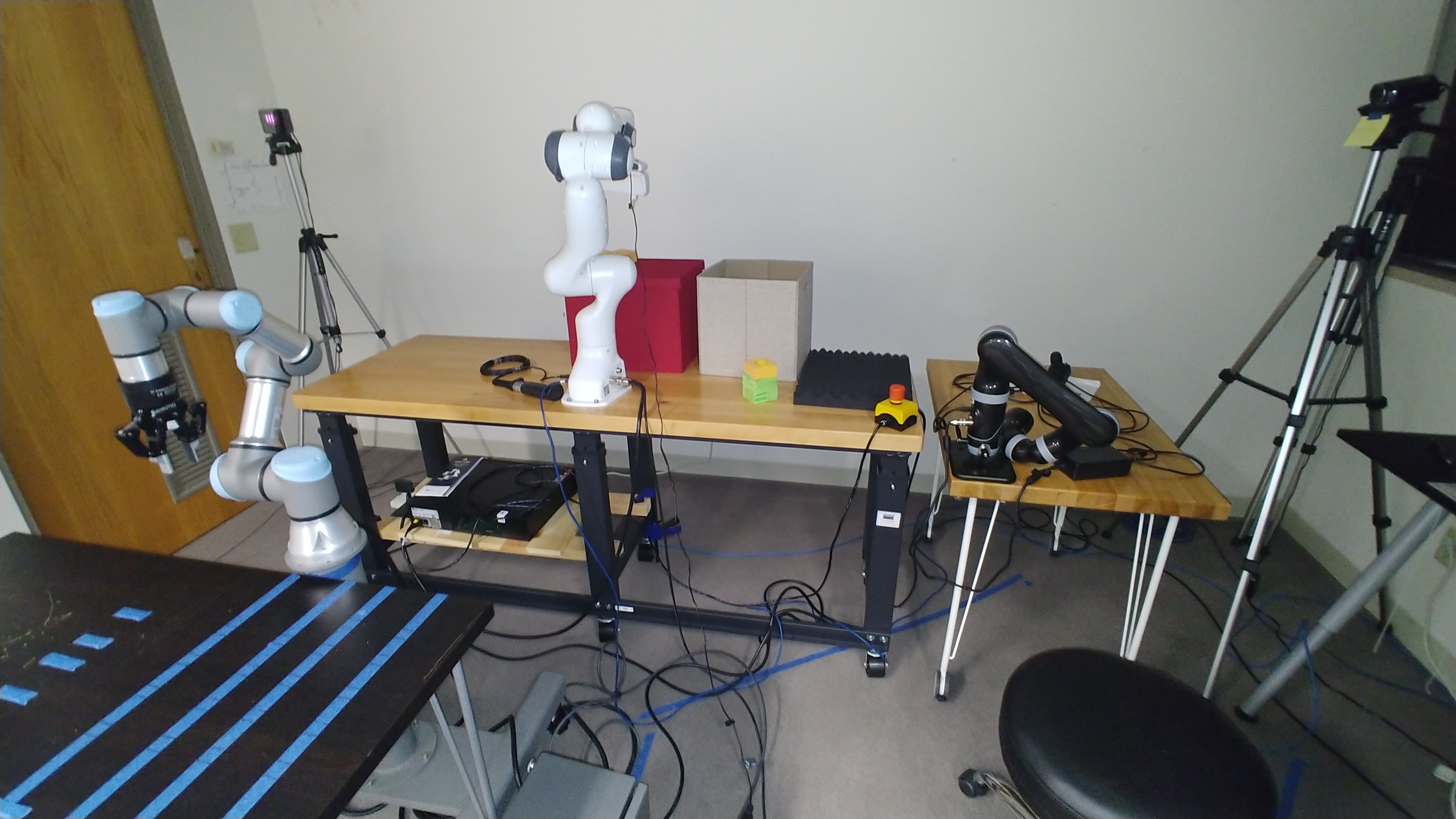 Lab experiment room with multiple robot arms (UR3e on the left, Franka Emkika Panda in the middle, Kinova Mico on the right).